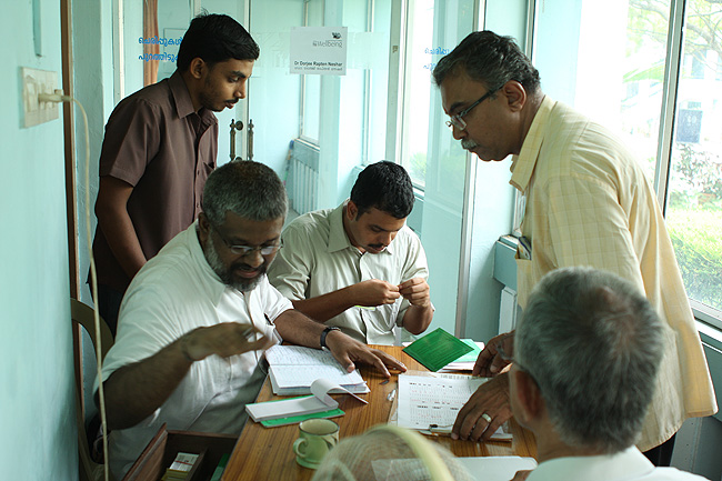Photograph of Rajsankar with Sethu Das, Sreejith Saseendran, Appu John and other Volunteers planning the rest of the camp and preparing Green Health Books for the newly-registered patients of December 2011. Once at the Wellbeing Camp venue Rajsankar needs to work with other Wellbeing Volunteers. He needs to verify the bookings and reports cancellations. He also needs to ensure that the entire team gets their consultation time with the doctors according to their booking preferences.