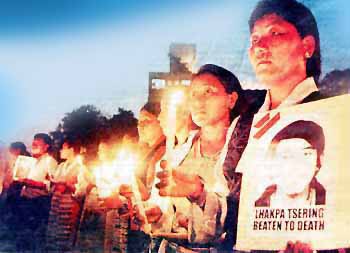 Tibetans in line of candle vigil, one holding sign:
        Lhakpa Tsering beaten to death'