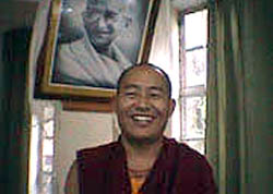 Venerable Yeshi Togden, smiling in front of photo of Mahatma Gandhi